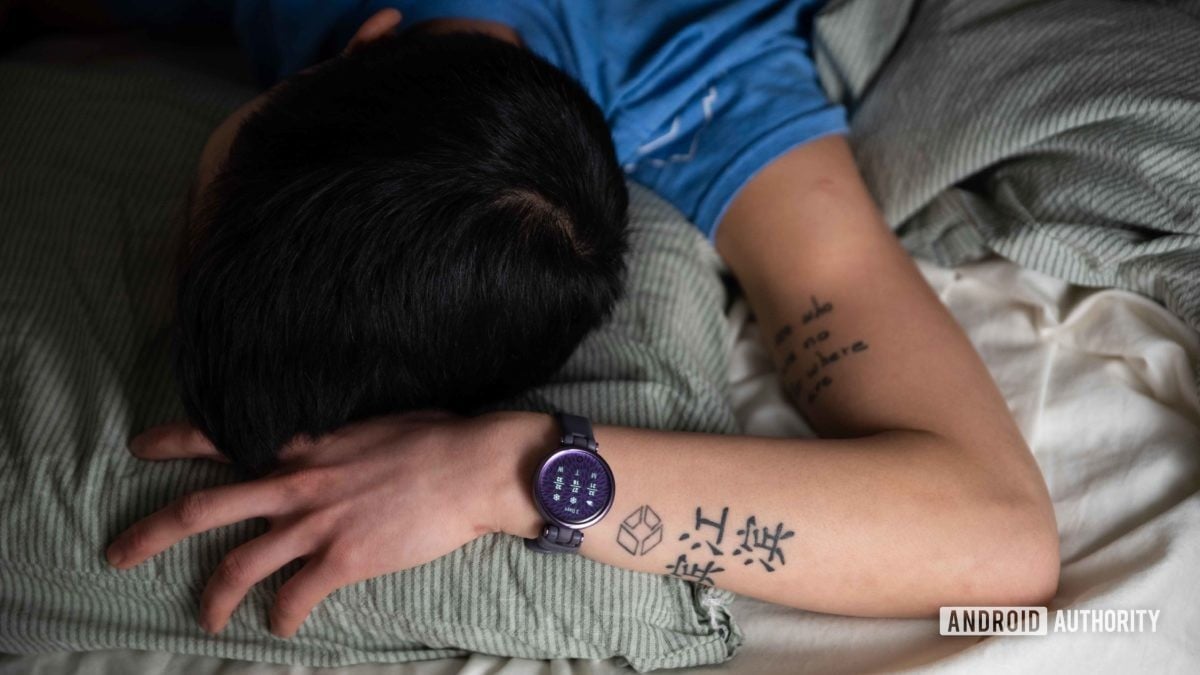 Ženska spi v postelji, medtem ko na levem zapestju nosi pametno uro Garmin Lily Sport Edition.