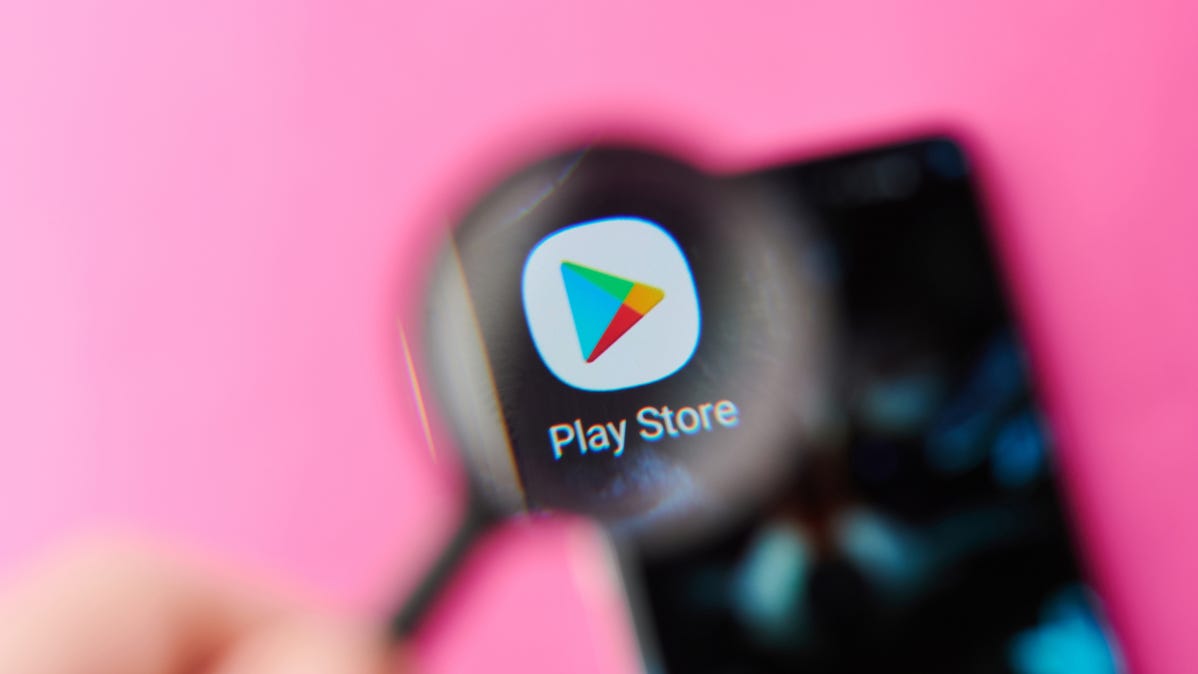 The Google Play Store logo on a smartphone shown through a magnifying glass