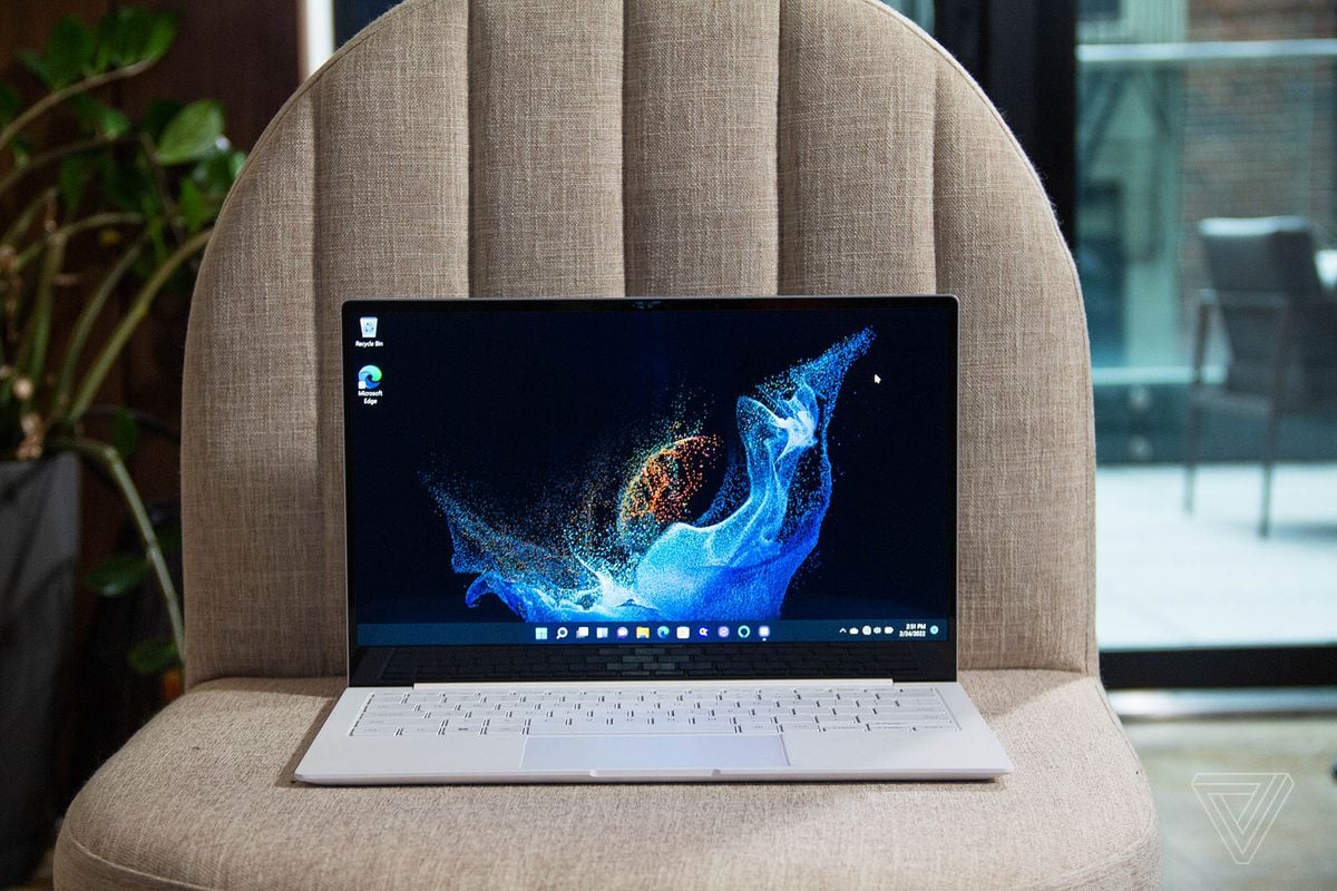 The Samsung Galaxy Book 2 Pro on a white plush chair with a houseplant in the background. The screen displays a blue supernova on a black background.