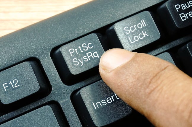A finger pressing the PrtSc key on the top row of a PC keyboard.