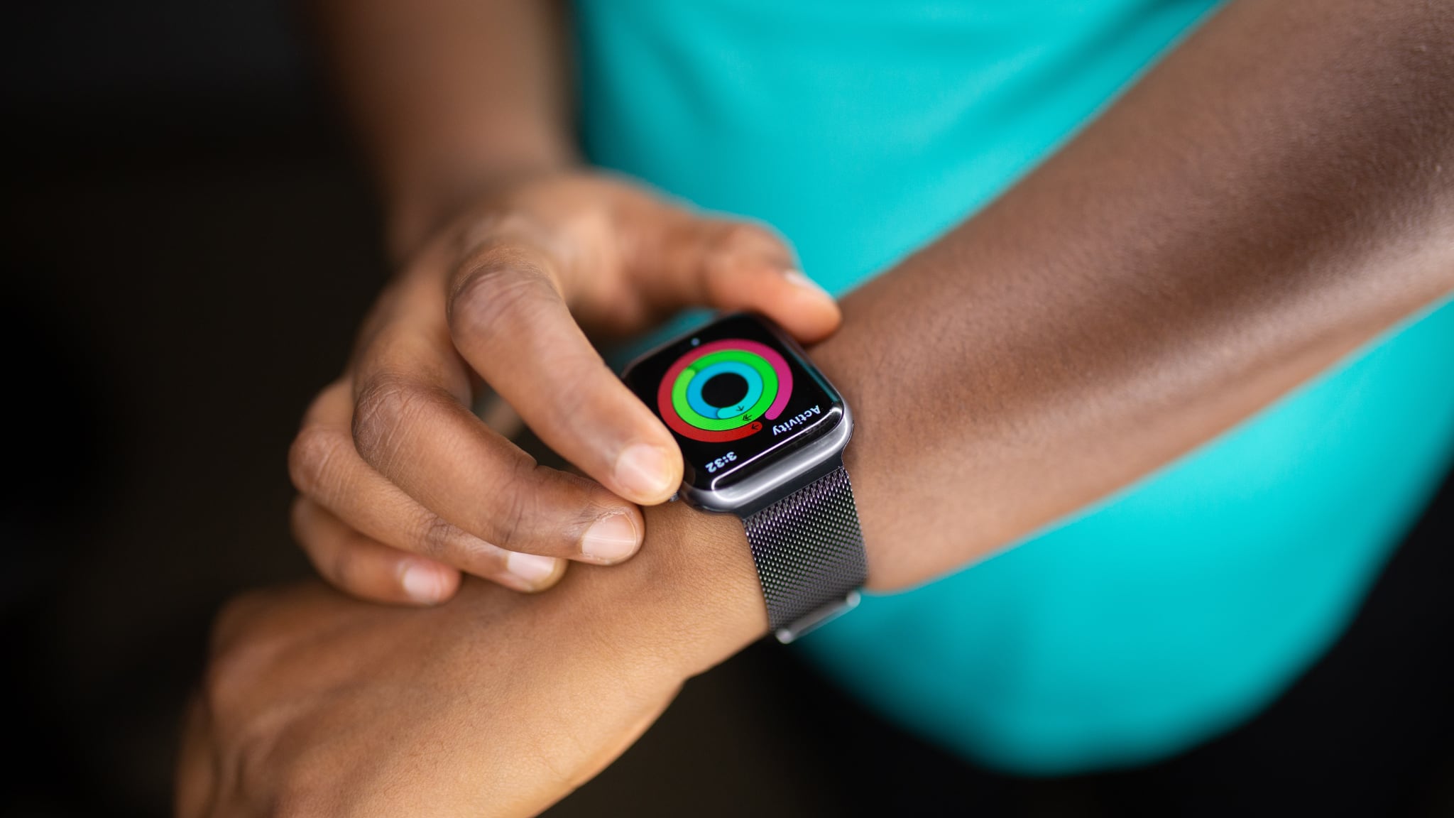 A closeup photograph of a female athlete's hand wearing an Apple Watch showing the Move, Exercise and Stand rings nearly closed