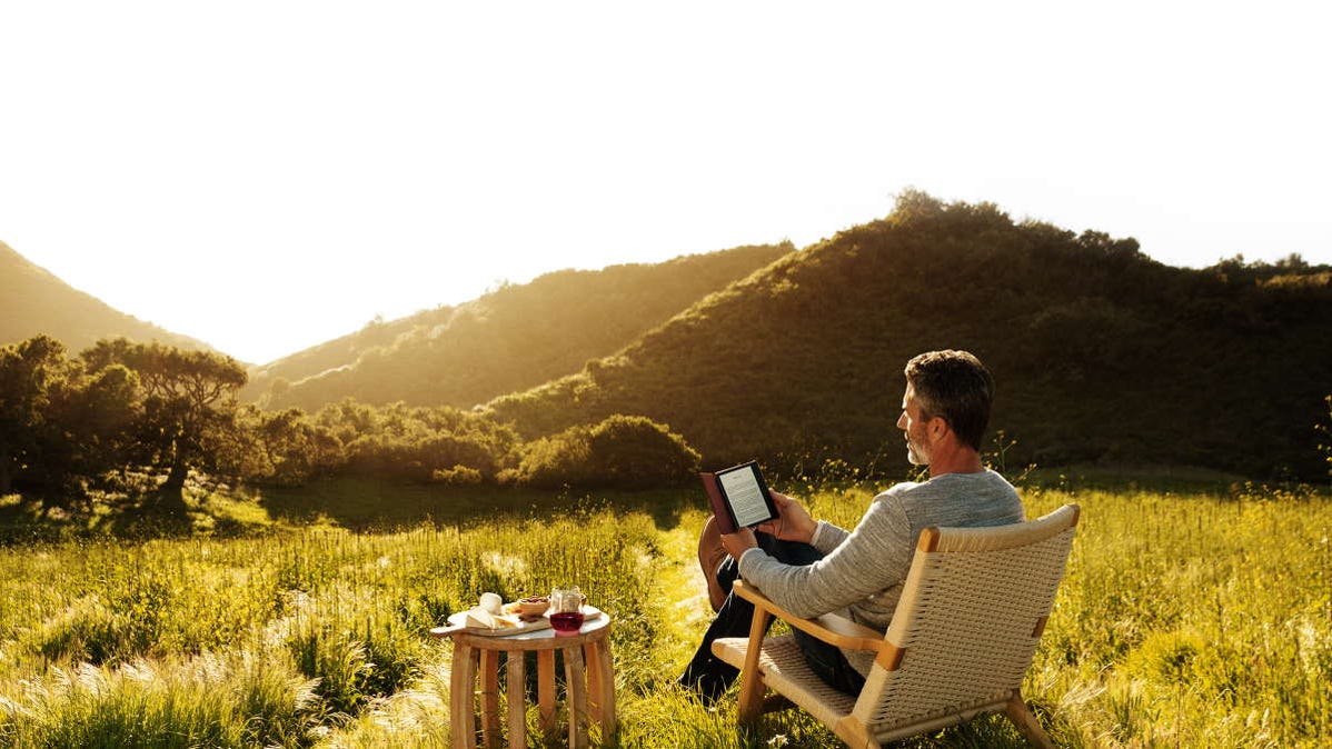 man reading kindle outside in hilly landscape