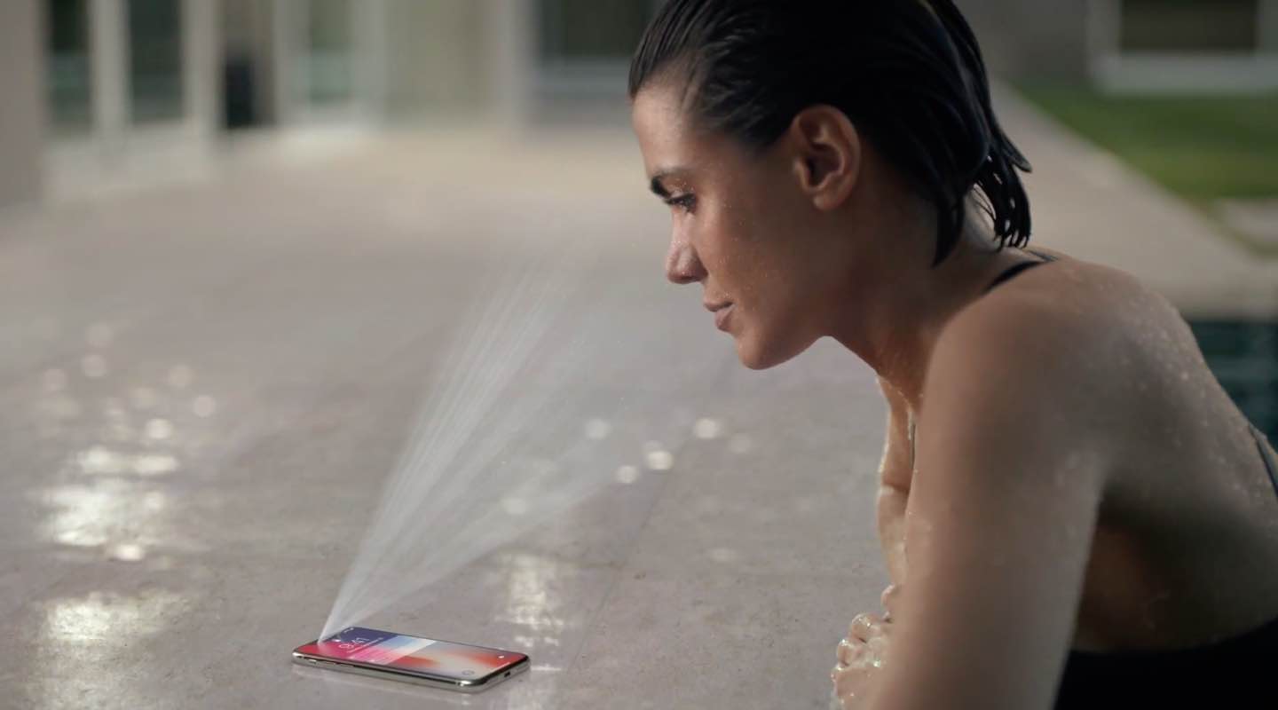 A still from Apple's iPhone X ad showing a woman by the poolside using Face ID to unlock her phone