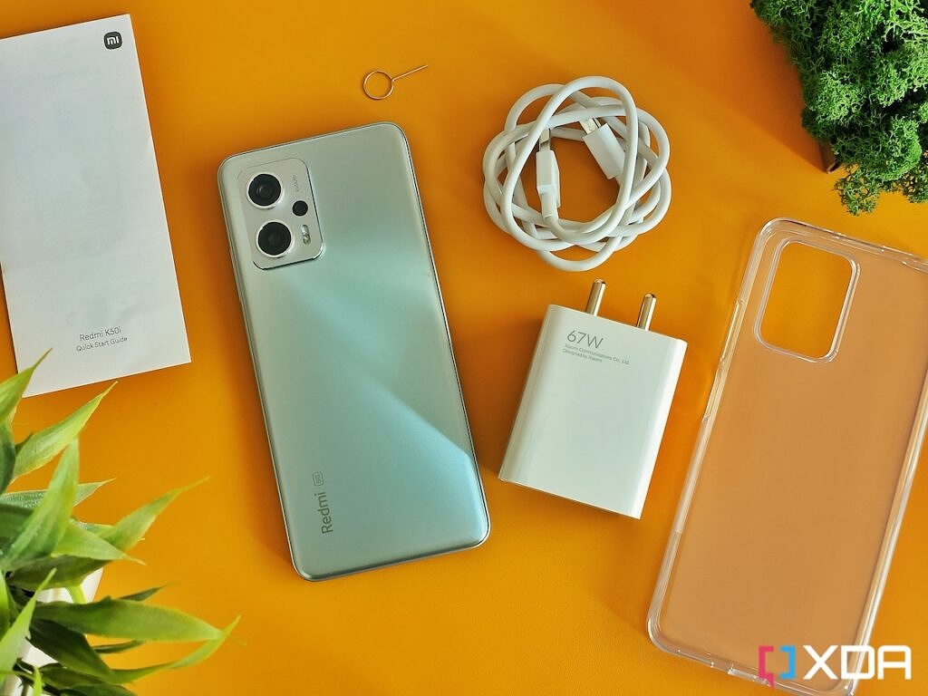 Redmi K50i smartphone in Silver color next to its retail box contents