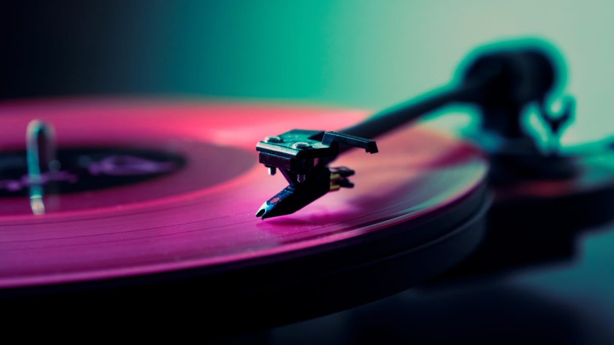 Closeup of a pink-colored record being played on a turntable.