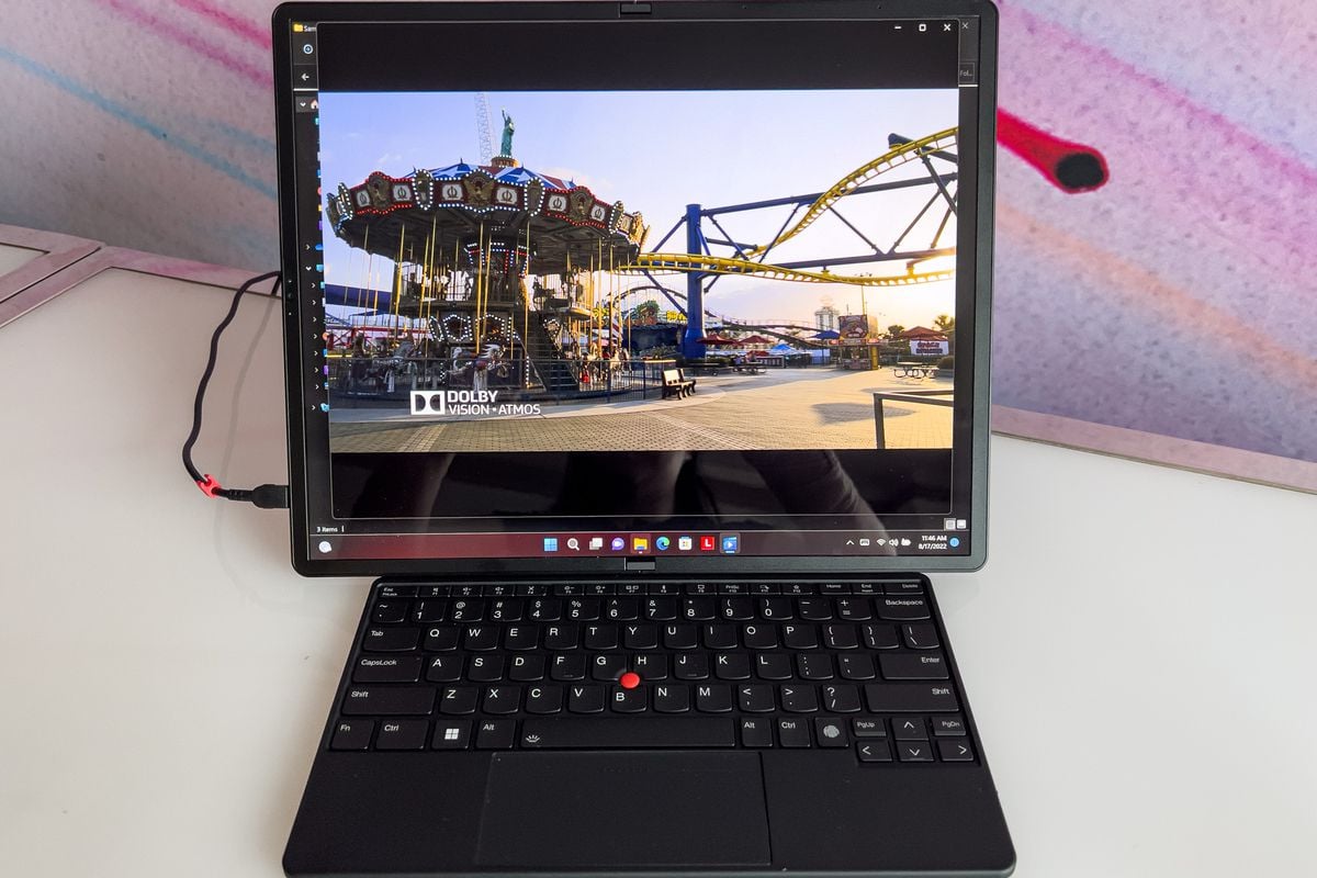 The ThinkPad X1 Fold in tablet mode with the bluetooth keyboard in a demonstration area. The screen displays a picture of a merry-go-round.