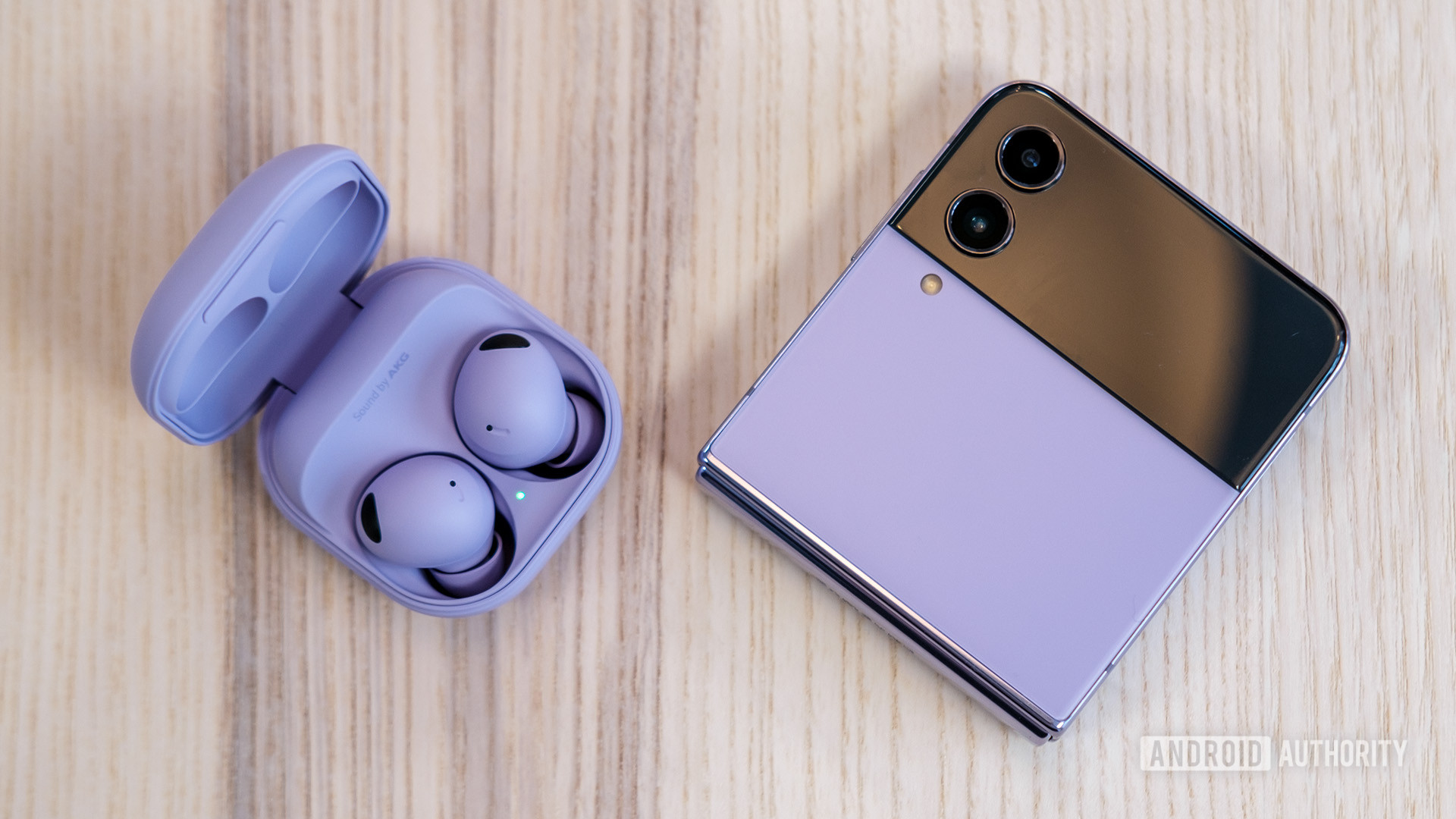 The Samsung Galaxy Buds 2 Pro in their case next to a Galaxy Z Flip 4 in a folded up position sitting on a wood table.
