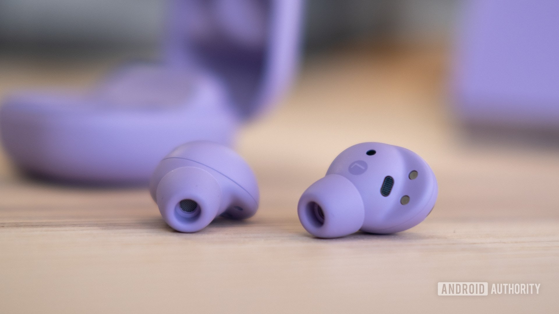The Samsung Galaxy Buds 2 Pro earbuds lying on a table with their case visible, though blurry, in the background.
