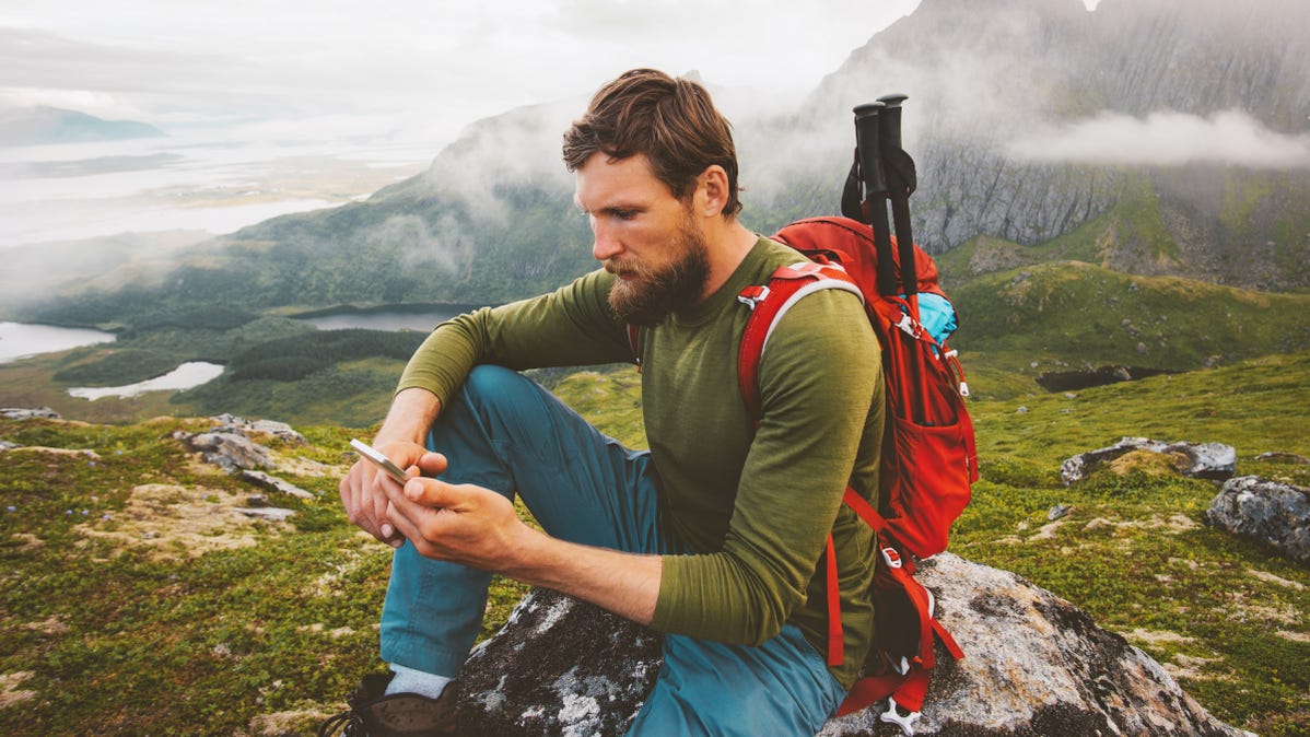 Man wearing a backpack and using a smartphone on top of a mountain.